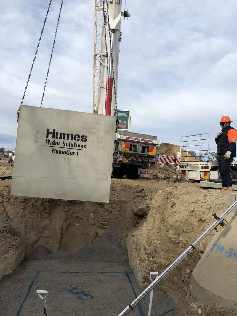 Crane lifting a precast HumeGard panel into an excavation, worker in hi-vis and hard hat watching from the edge