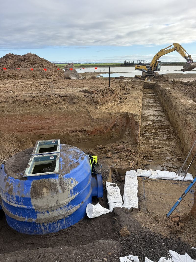 Blue GPT (gross pollutant trap) unit beside a freshly dug trench, excavator working in the background