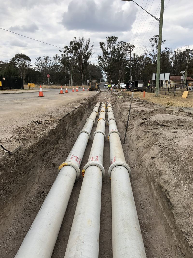 Three parallel concrete stormwater pipe lines laid in a trench beside a road