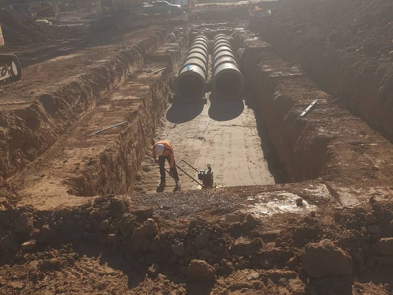 Twin large-diameter RCP stormwater lines in a wide cut, pipe crew in hi-vis working at a distance