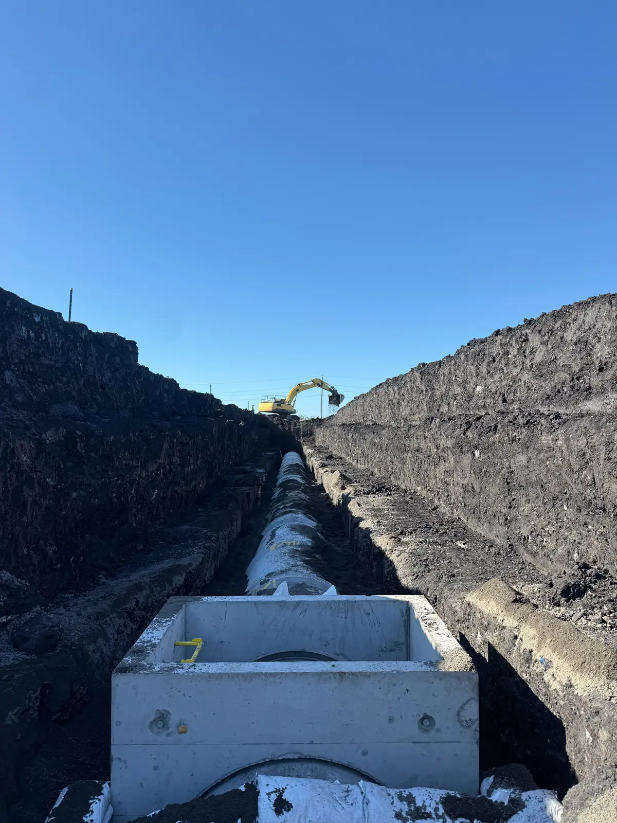 Precast pit and stormwater pipe run in a deep trench, excavator in the background